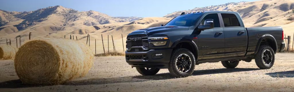 Black RAM pickup truck parked on a rural landscape next to a hay bale.