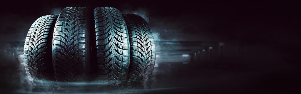 Set of four vehicle tires with deep treads against a dark, smoky background.