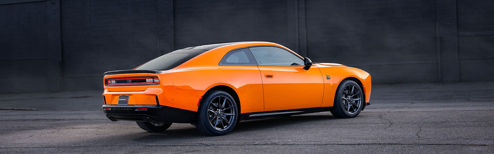 Bright orange Dodge Charger sports coupe parked against a dark wall.