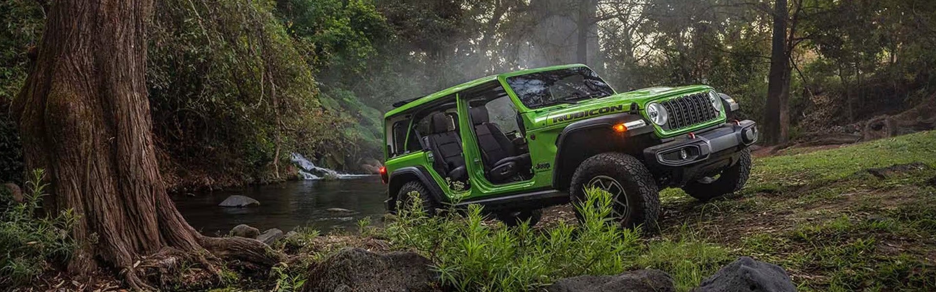 Bright green doorless Jeep Wrangler parked by a forest stream.