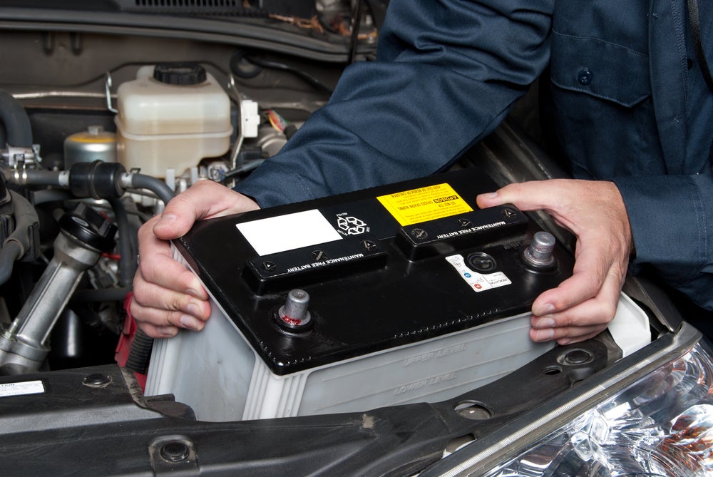 Vehicle battery being installed under the hood by an automotive technician.